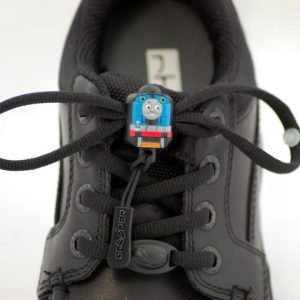 Image is a photograph of a pair of smart, black school shoes with black Greeper dress laces featuring a small Thomas the Tank Engine emblem in the center