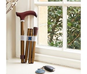 Image is a photograph of a bronze-coloured walking stick with wooden handle, folded neatly and placed upright on a windowsill next to a set of car keys