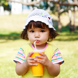 Image of a brown-haired toddler in a sunny garden, drinking from a cup using a straw