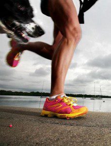 Image of a man running next to a lake with his dog, wearing brightly coloured trainers and greeper laces.