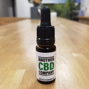 Image is a photograph of a tincture bottle of Hybrid CBD oil on a wooden table