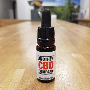 Image is a photograph of a tincture bottle of Sativa CBD oil on a wooden table